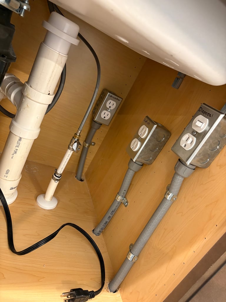 Under-sink plumbing with water filter, curved pipe, electrical outlets, and drain connections mounted on wooden cabinet interior