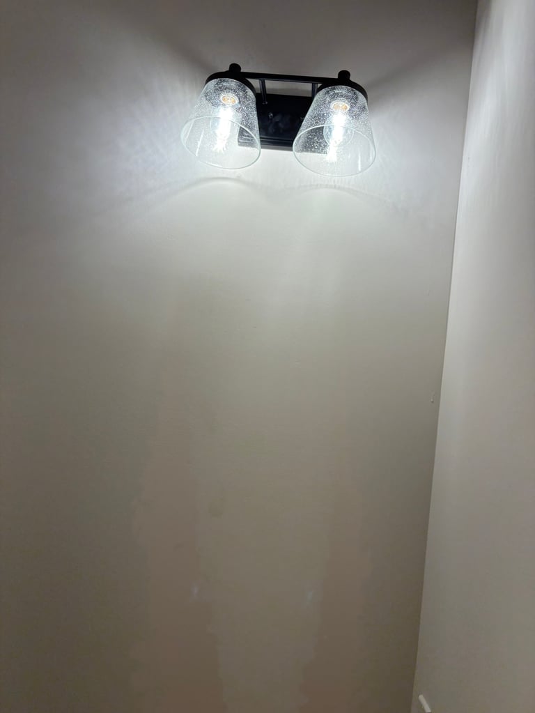 Black dual vanity light fixture mounted on white wall with two clear glass shades and LED bulbs illuminated